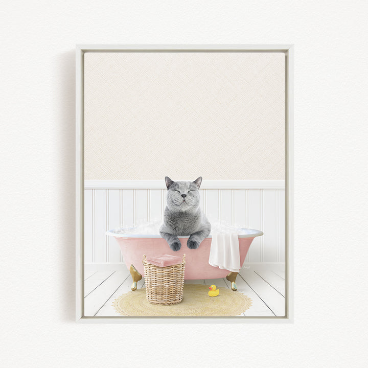 A gray cat sitting in a pink bathtub, surrounded by a yellow rubber duck and a wicker basket.