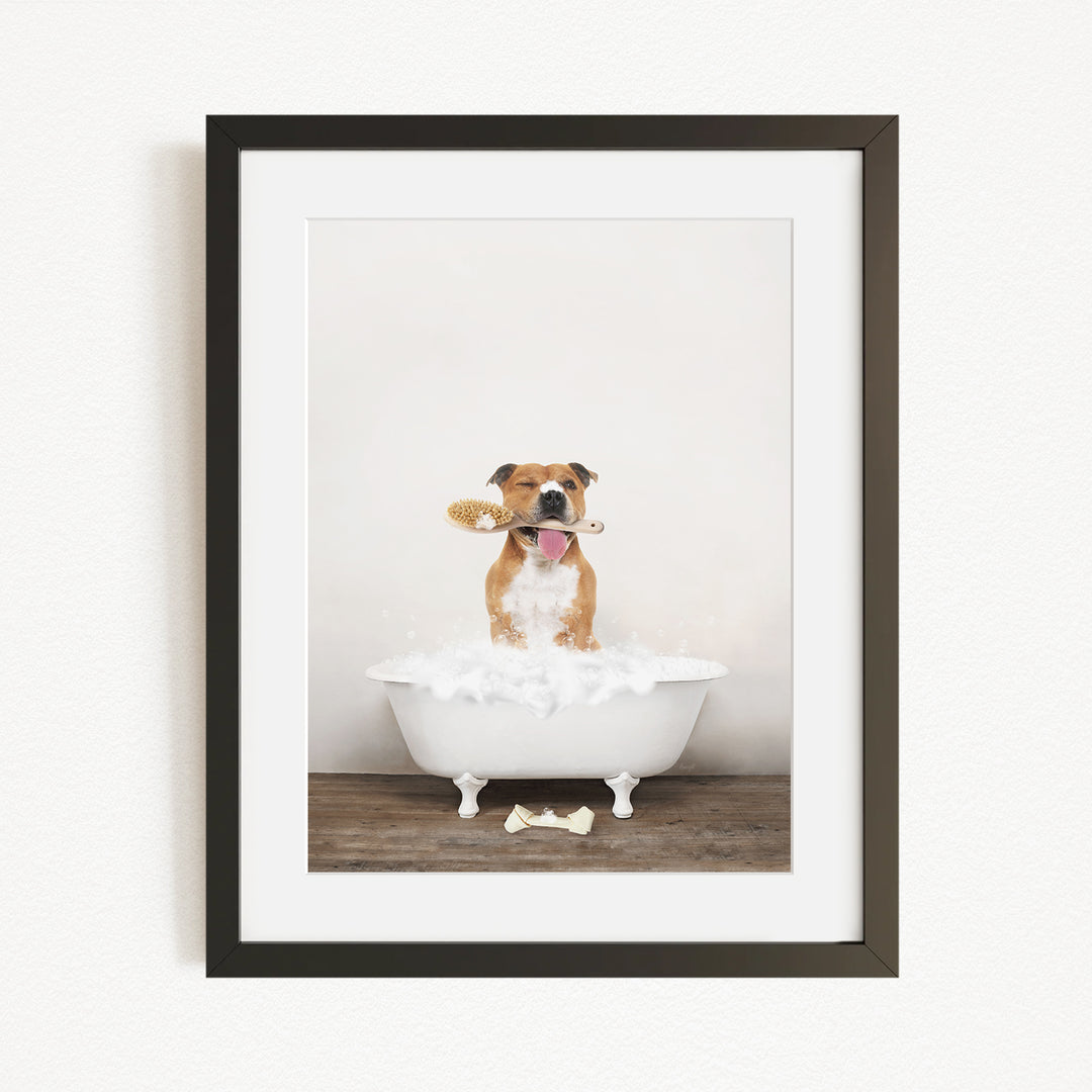A brown and white dog sitting in a white bathtub, holding a brush in its mouth, with a bone on the floor.