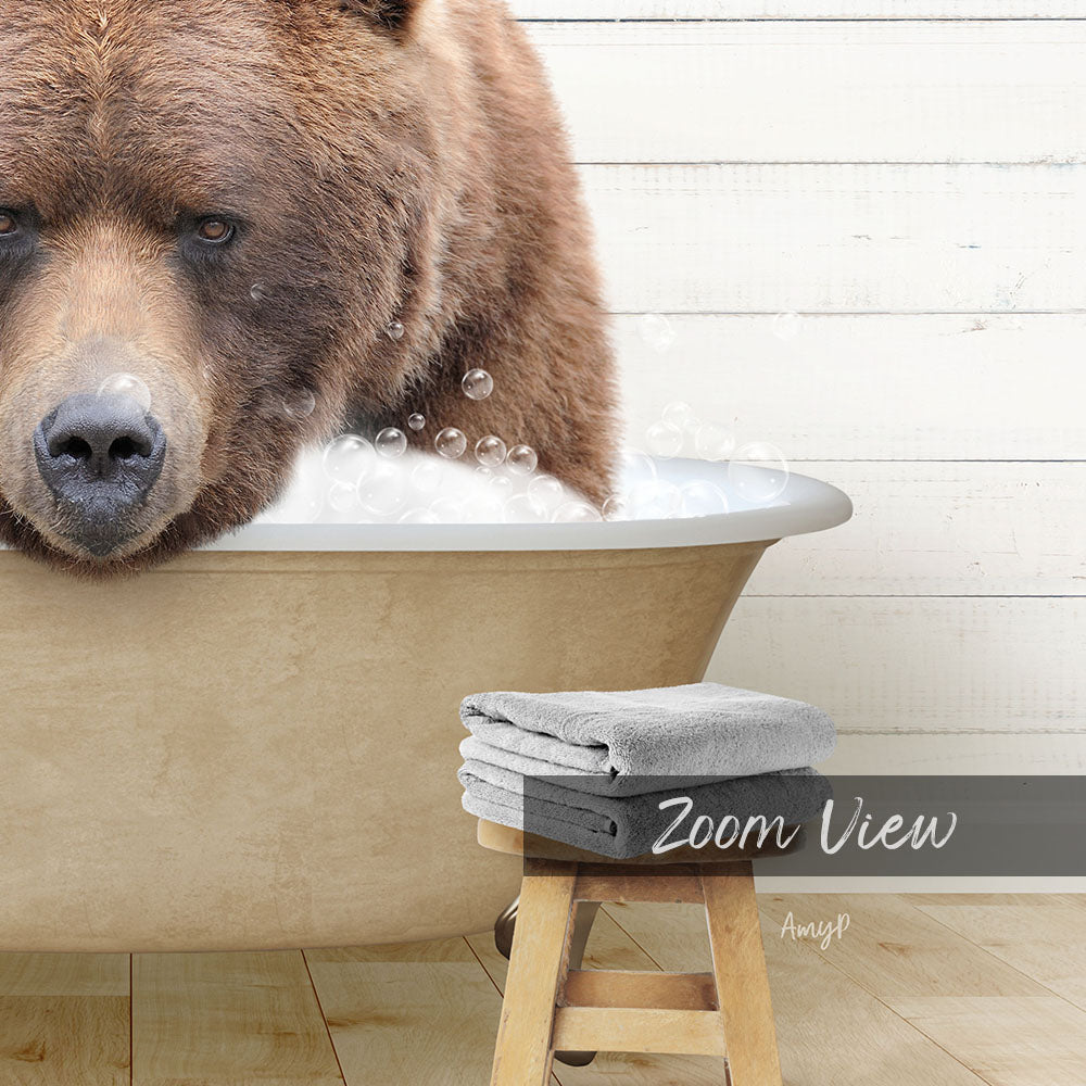 A large brown bear is sitting in a bathtub filled with bubbles, with a towel and stool visible in the foreground.