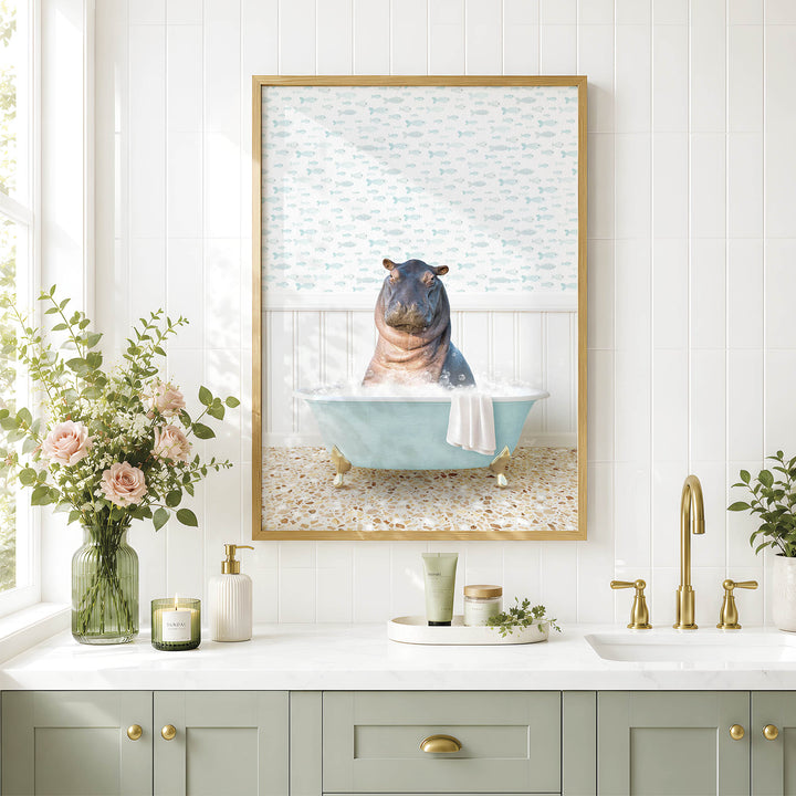 A framed image of a hippopotamus sitting in a bathtub, surrounded by a blue bathtub, a white towel, and a vase of pink flowers, is displayed on a white tiled wall above a bathroom sink.