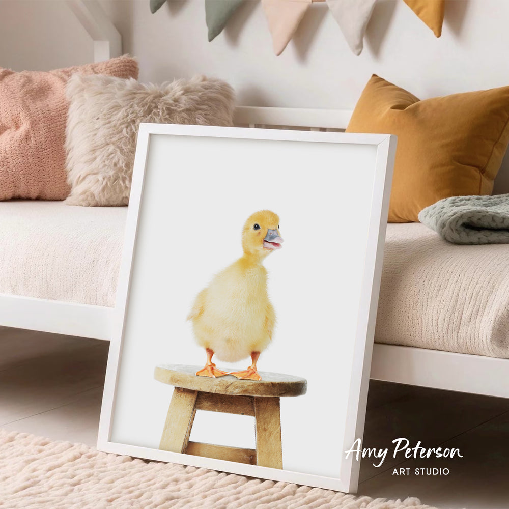 A framed image of a yellow duck standing on a wooden stool, with a cozy and colorful background.