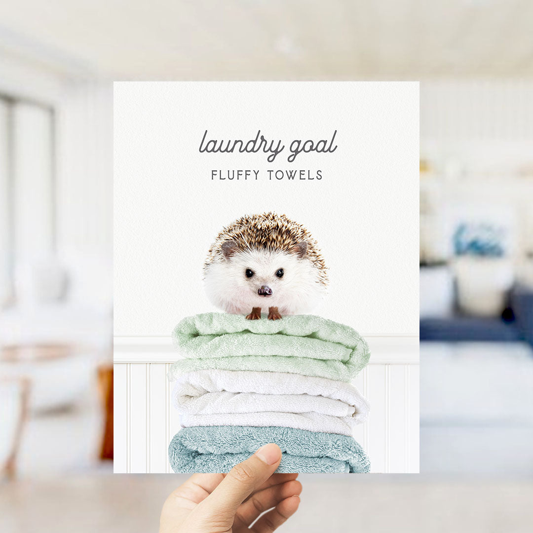 A hand holding a stack of fluffy towels with a hedgehog sitting on top.