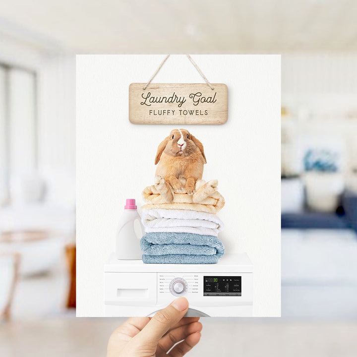 A hand holding a white laundry machine with a sign above it that says "Laundry Goal Fluffy Towels".