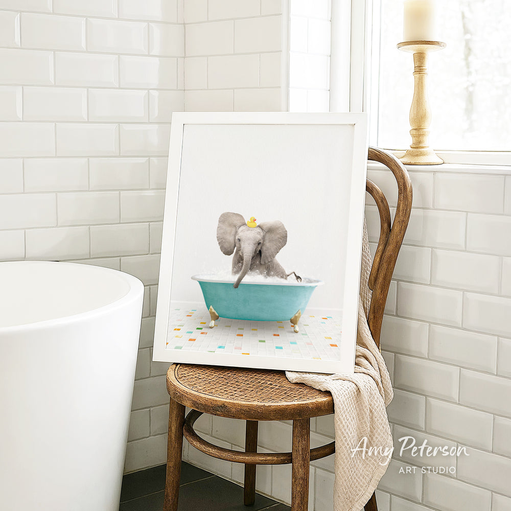 A framed image of an elephant sitting in a blue bathtub, surrounded by colorful tiles, is displayed on a wooden chair in a bathroom setting.