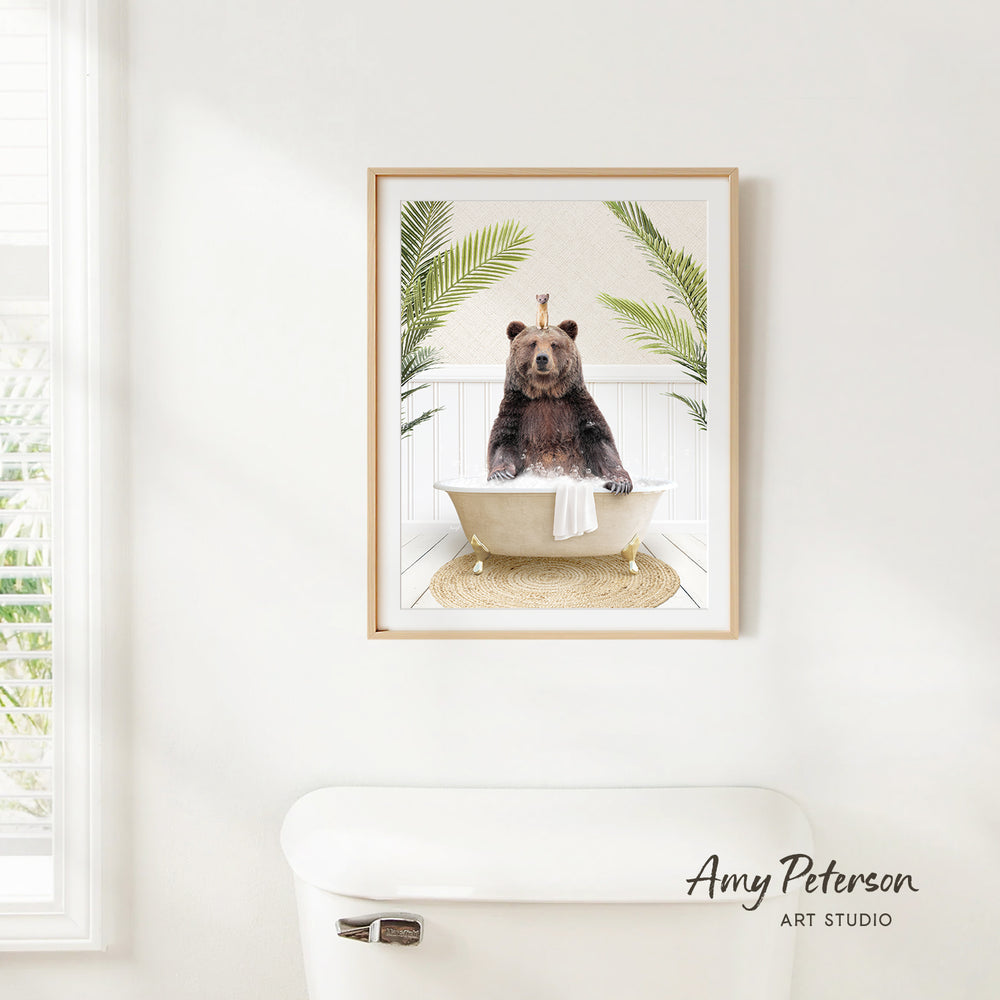 A framed image of a bear sitting in a bathtub, surrounded by palm leaves, is hanging on a white wall.