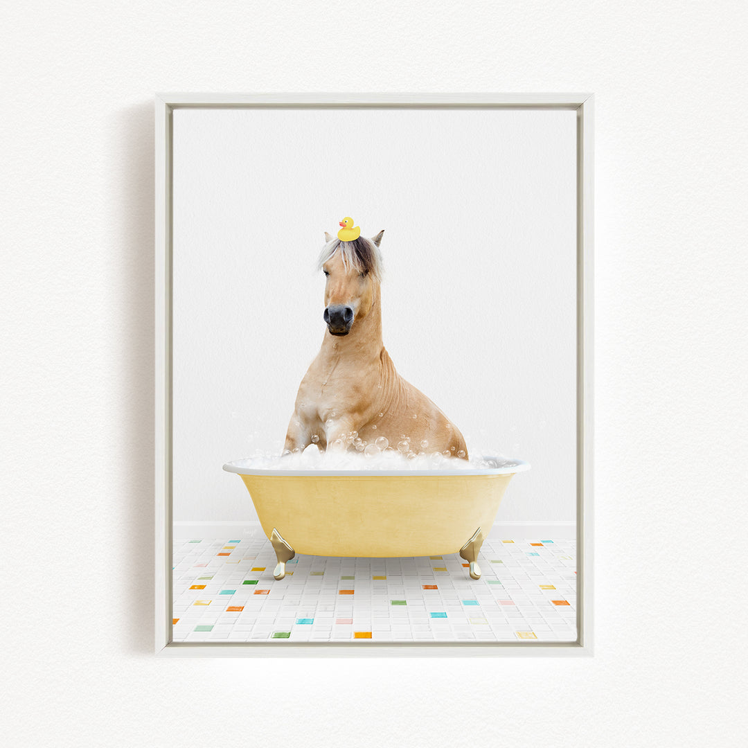 A light brown horse is sitting in a yellow bathtub filled with bubbles, wearing a yellow rubber duck on its head.
