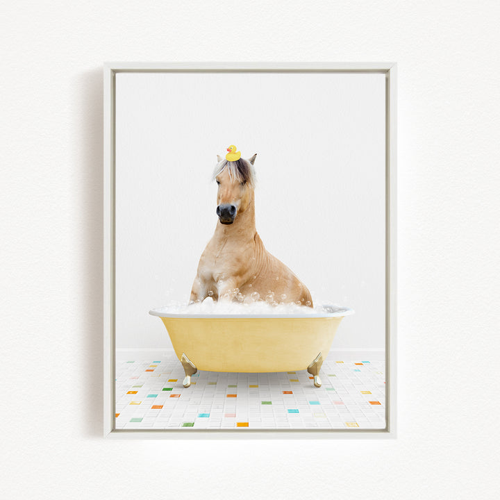 A light brown horse is sitting in a yellow bathtub filled with bubbles, wearing a yellow rubber duck on its head.