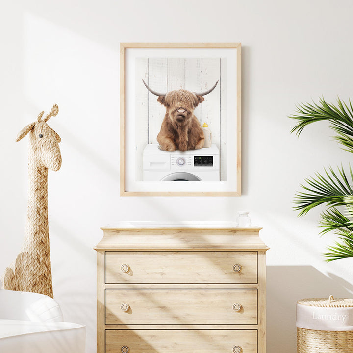 a framed photograph of a Highland cow sitting on top of a washing machine, with a giraffe figurine next to it.