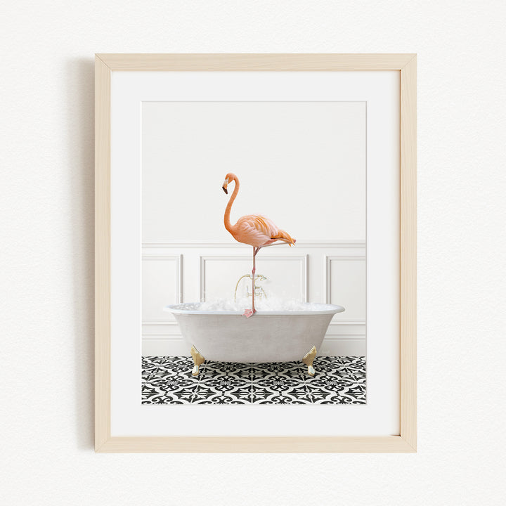 A framed image of a pink flamingo standing in a white bathtub filled with water, set against a white wall with a black and white patterned floor.