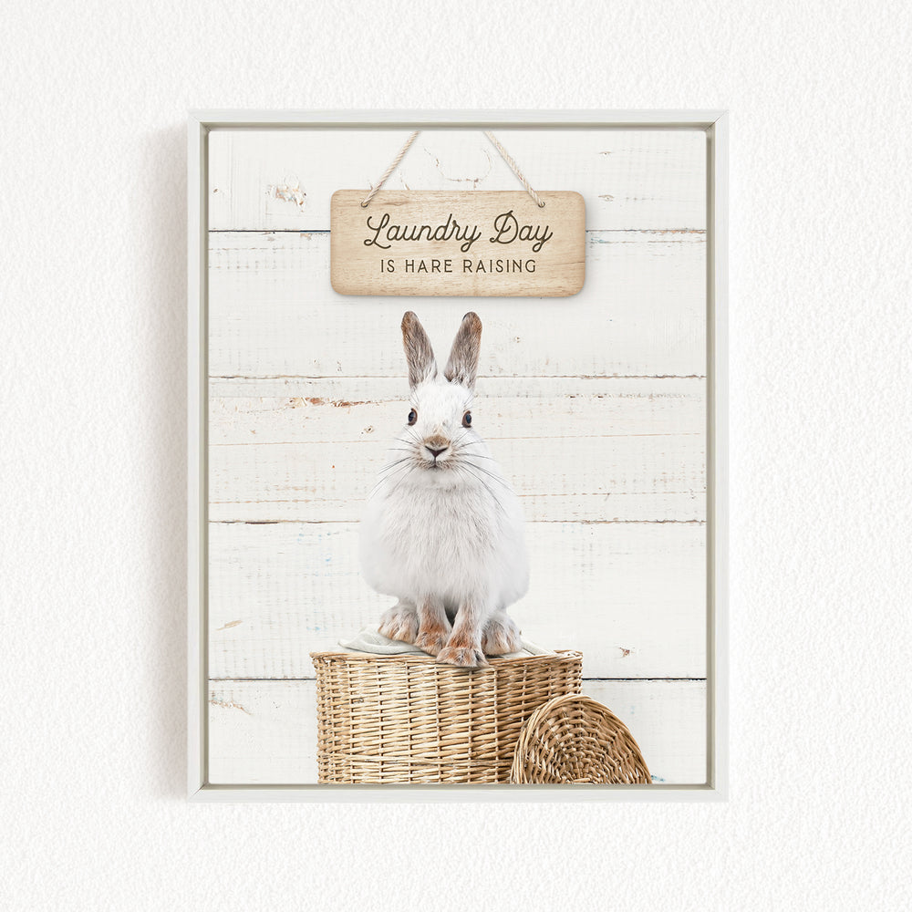 A white rabbit sitting on a wicker basket, with a wooden sign above that says "Laundry Day is HARE RAISING".