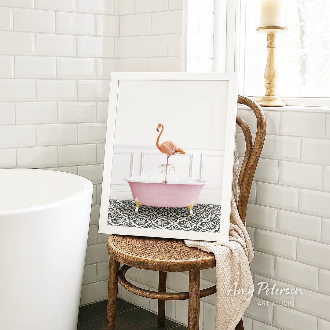 A framed image of a pink flamingo sitting in a pink bathtub is displayed on a wooden chair in a bathroom setting.