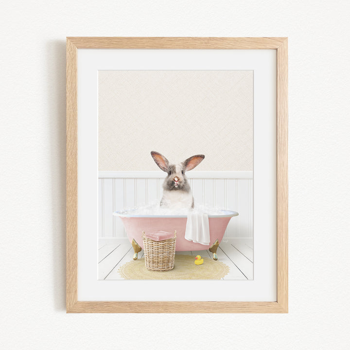 A small rabbit sitting in a pink bathtub filled with water, surrounded by a yellow rubber duck and a basket.