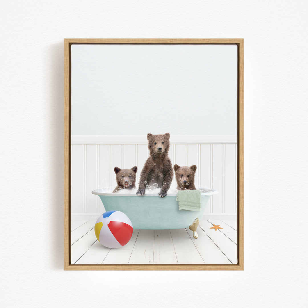 A framed image depicting three brown bears sitting in a bathtub, with a beach ball and towel nearby.