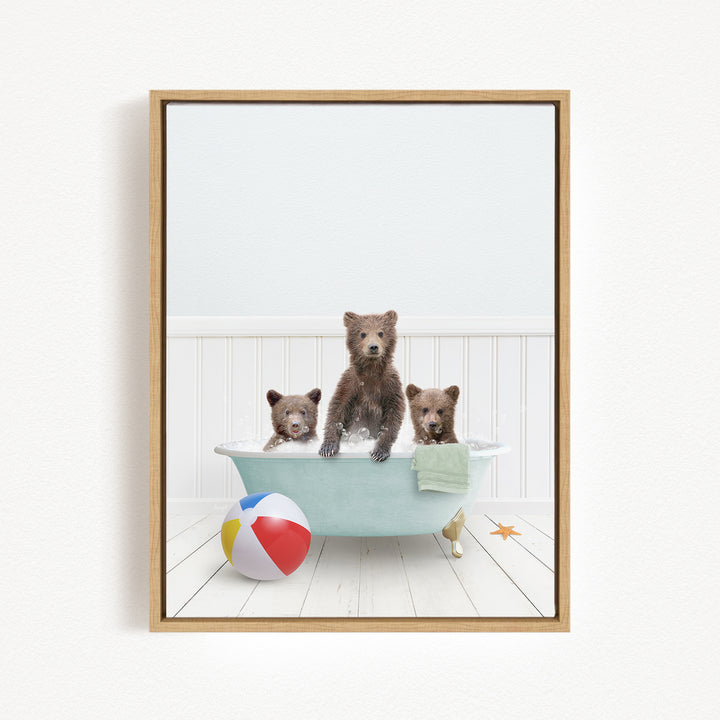 A framed image depicting three brown bears sitting in a bathtub, with a beach ball and towel nearby.