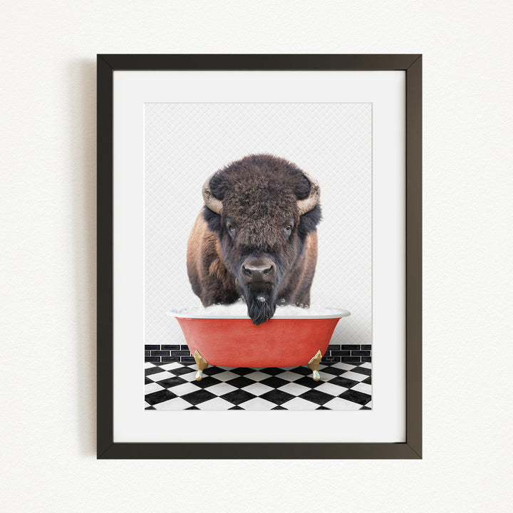 A buffalo with large horns is standing in a red bathtub, with a black and white checkered floor beneath it.
