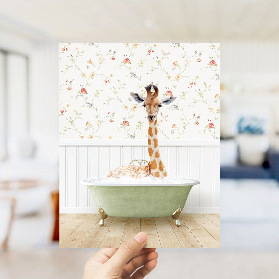 A giraffe sitting in a green bathtub filled with bubbles, with a floral wallpaper in the background.