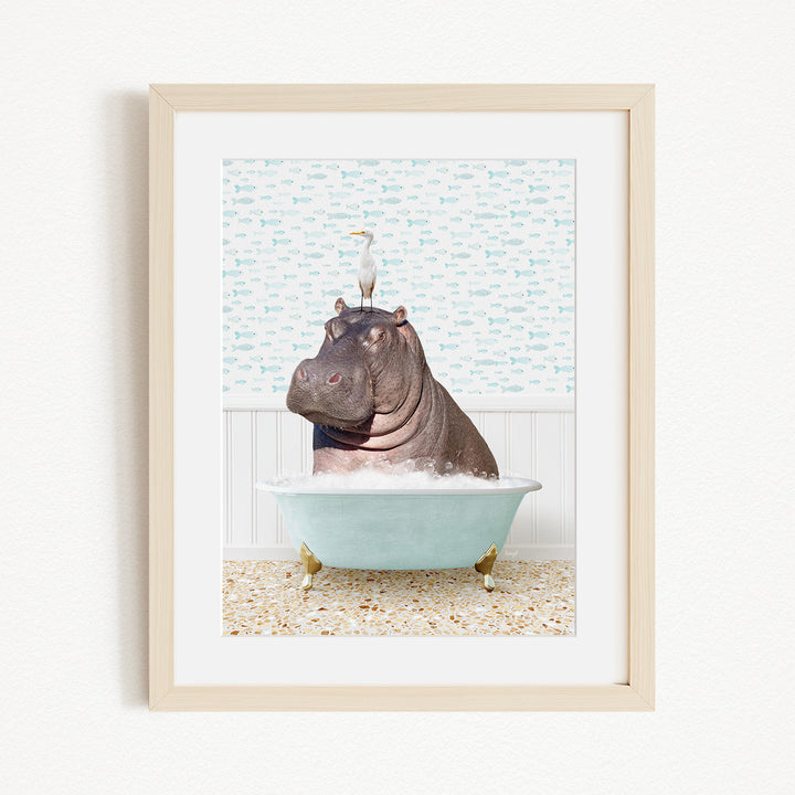 A framed image depicting a hippopotamus sitting in a bathtub, with a bird perched on its head.