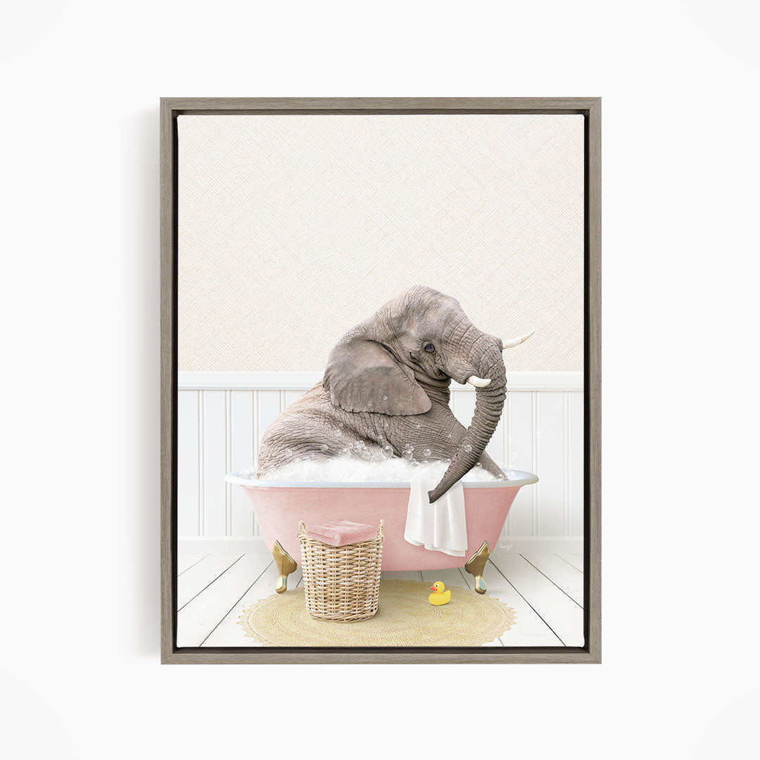 A gray elephant is sitting in a pink bathtub filled with water, surrounded by a yellow rubber duck and a basket of bath toys.