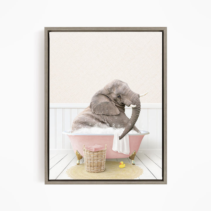 A gray elephant is sitting in a pink bathtub filled with water, surrounded by a yellow rubber duck and a basket of bath toys.