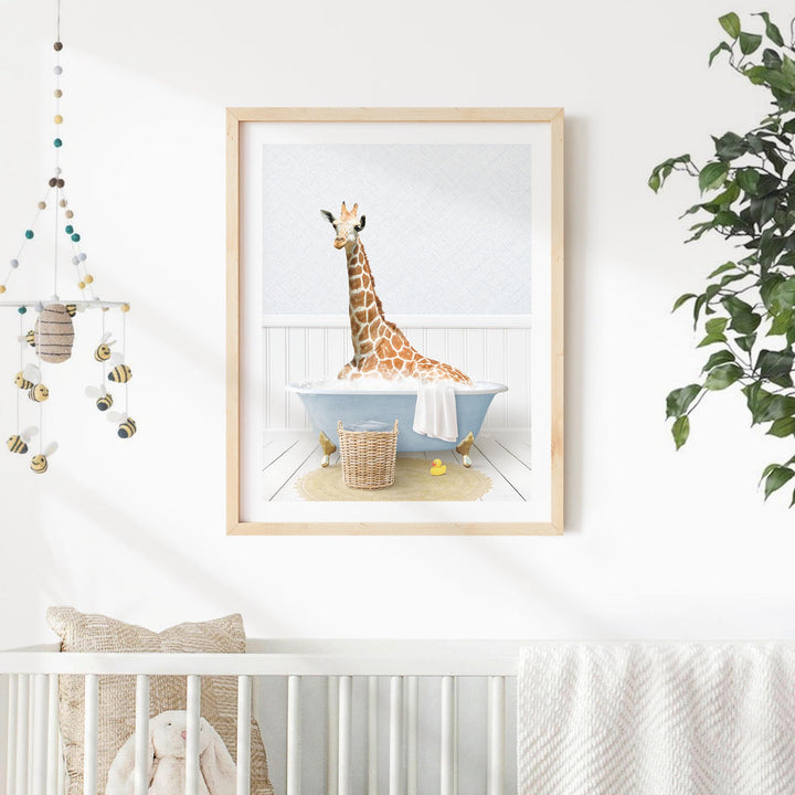 A giraffe sitting in a blue bathtub, surrounded by a basket of toys and a hanging mobile, in a nursery setting.