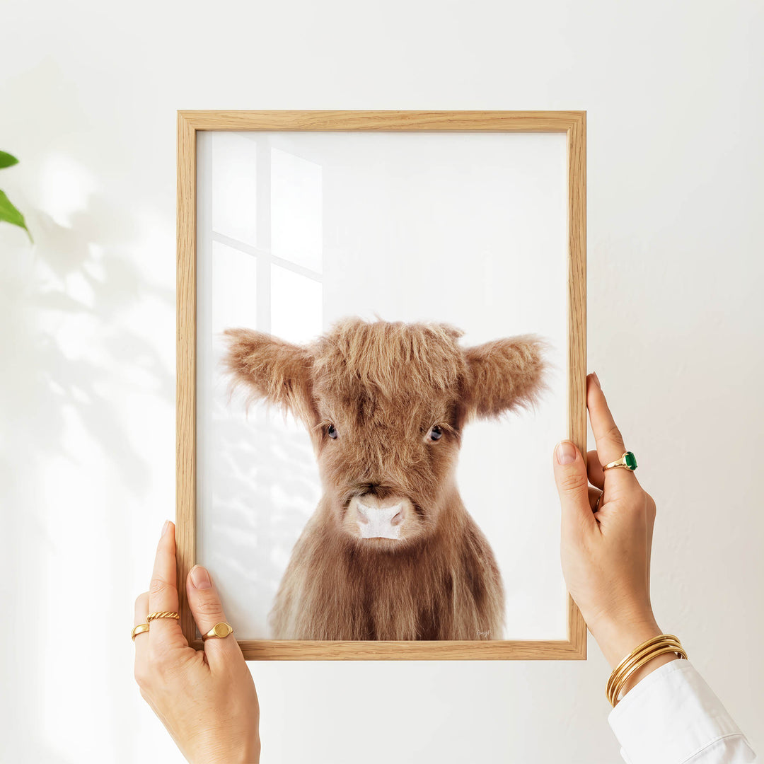 A person's hands are holding a wooden frame with a picture of a brown cow inside it.