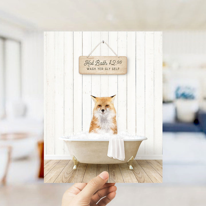 A hand holding a framed image of a cat sitting in a bathtub, with a sign above it that says "Hot Bath $2.00 WASH YER LITTEL SELF".