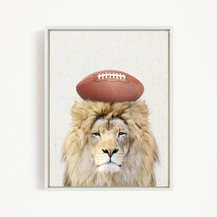 A lion with a football on its head, looking directly at the camera.