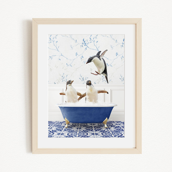 A framed image depicting two penguins sitting in a blue bathtub, with one penguin jumping out of the tub.