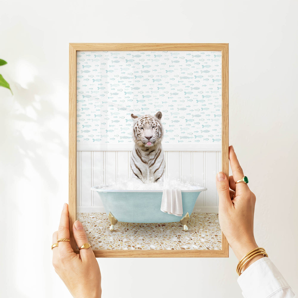 A person's hands are holding a framed image of a tiger sitting in a bathtub filled with water and bubbles.