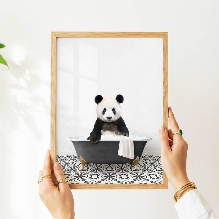 A person's hands are holding a picture frame containing a photograph of a panda bear sitting in a bathtub.
