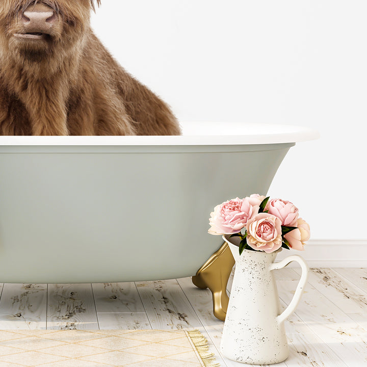 A brown cow is sitting in a green bathtub, with a vase of pink flowers next to it on a white floor.