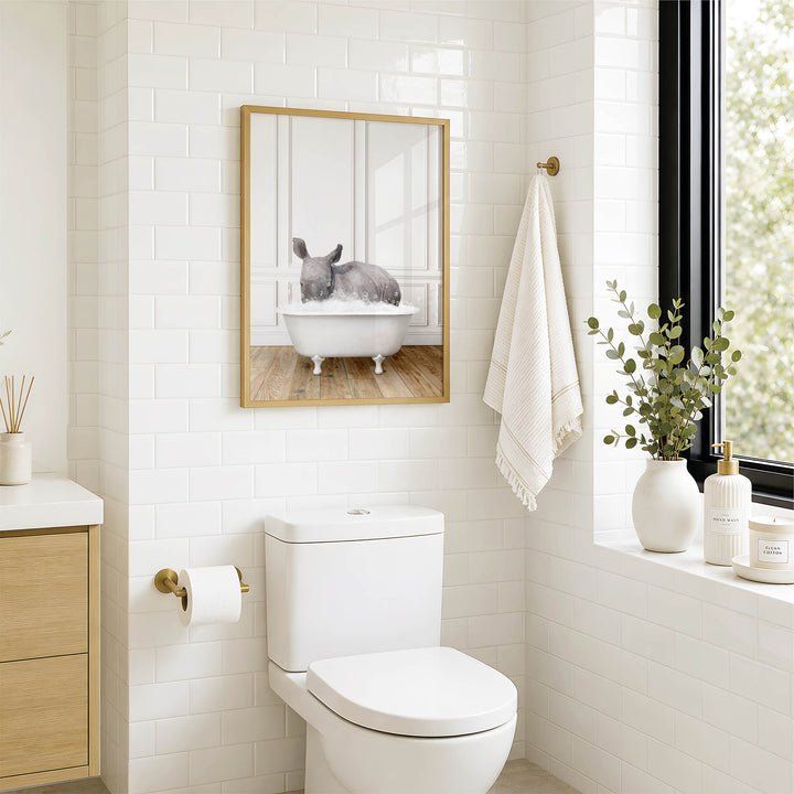 A bathroom with a white toilet, a framed image of a rabbit in a bathtub, and a window with greenery on the sill.