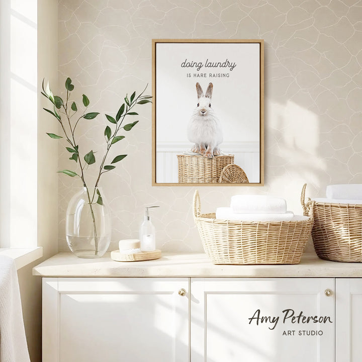 a bathroom with a framed picture of a rabbit on a basket, a vase with green leaves, and baskets on a counter.