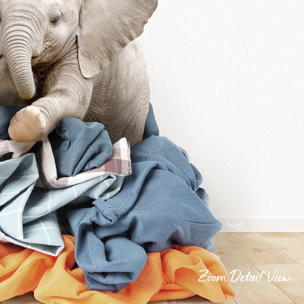 A baby elephant sitting on a pile of clothes, with a white wall in the background.