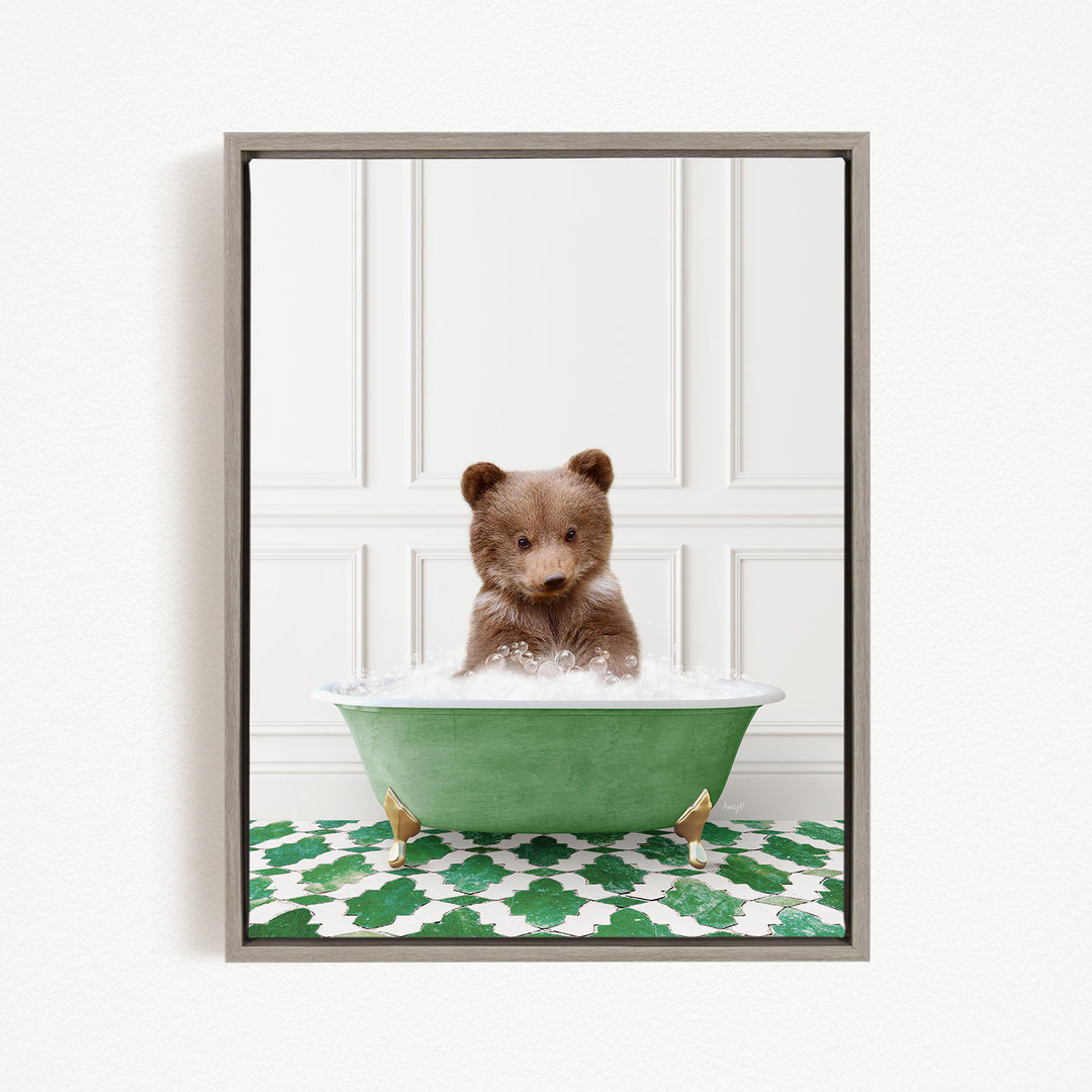 A cute brown bear cub sitting in a green bathtub filled with water, surrounded by a green and white patterned mat.