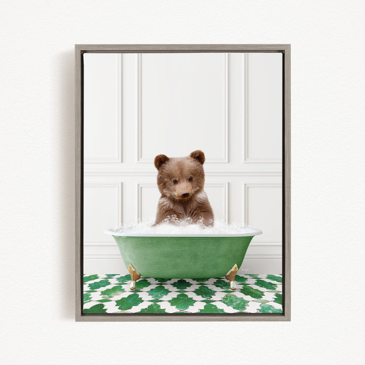 A cute brown bear cub sitting in a green bathtub filled with water, surrounded by a green and white patterned mat.