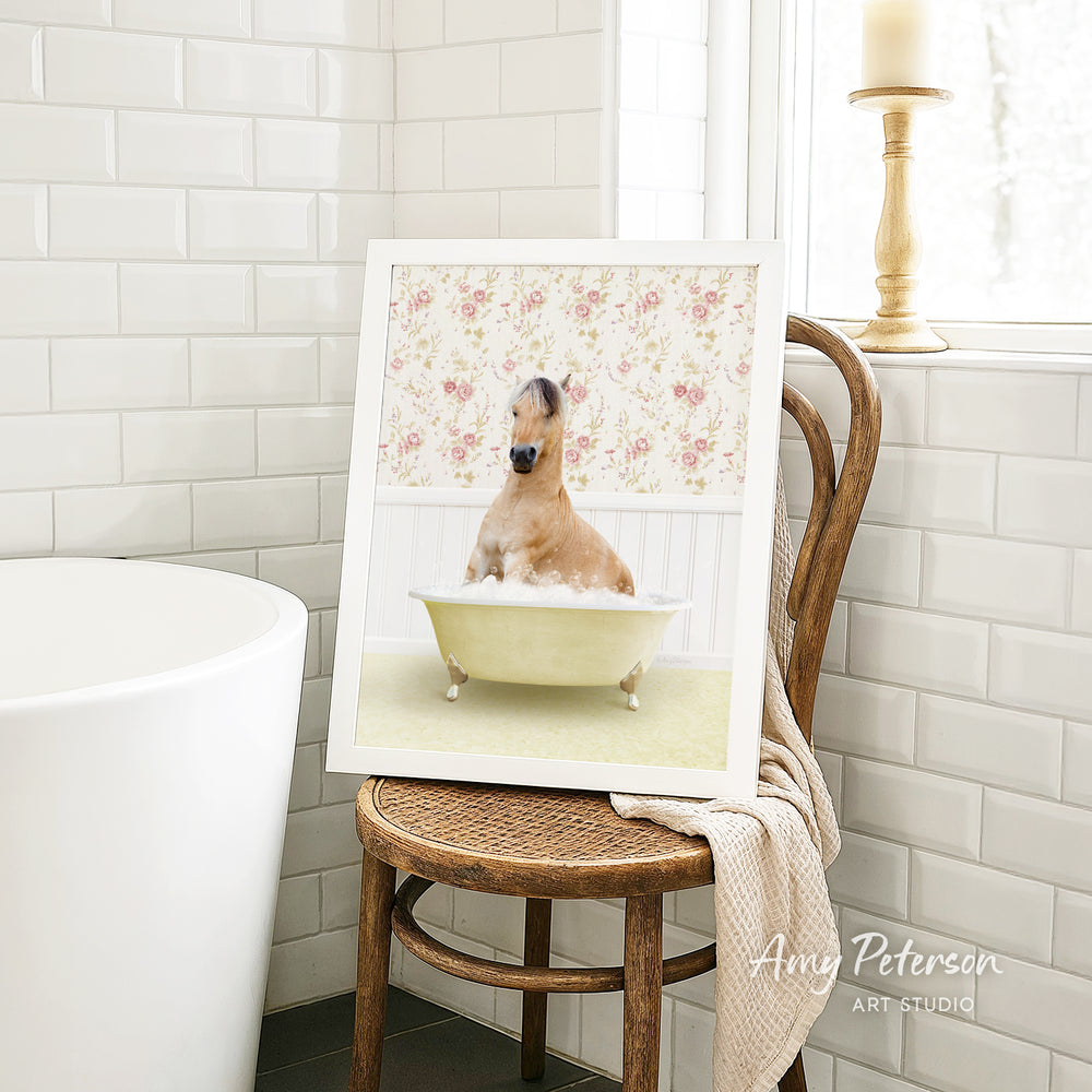 A framed image of a dog sitting in a bathtub, surrounded by a floral pattern, is displayed on a wooden chair in a bathroom setting.