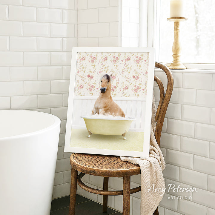 A framed image of a dog sitting in a bathtub, surrounded by a floral pattern, is displayed on a wooden chair in a bathroom setting.