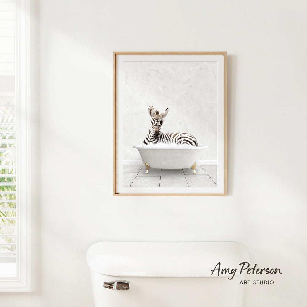 A framed image of a zebra sitting in a bathtub is hanging on a white wall.