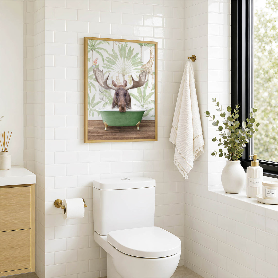 A bathroom with a white toilet, a framed picture of a moose in a bathtub, and a window with greenery on the sill.