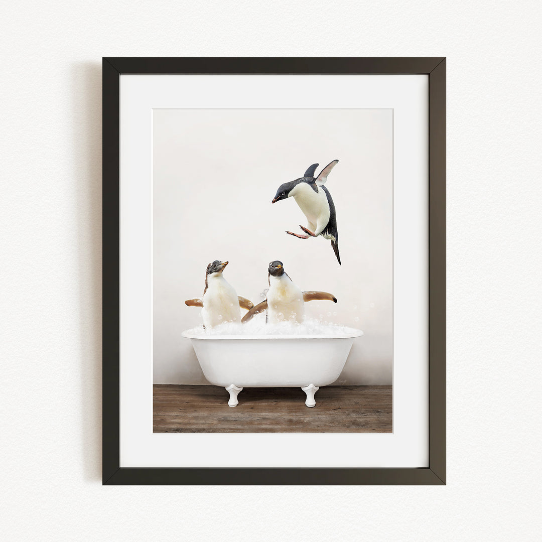 A framed image depicting two penguins sitting in a white bathtub, with one penguin flying towards the other.