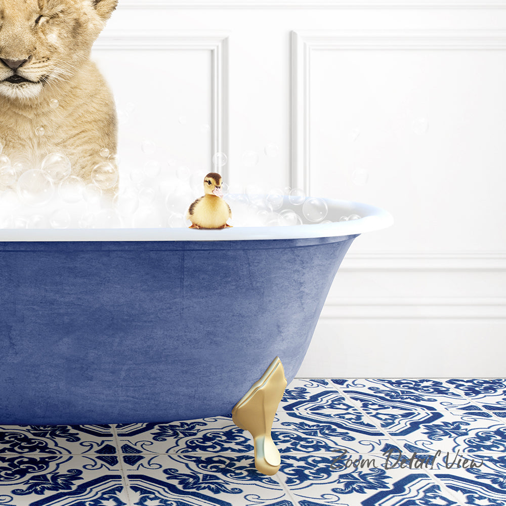 A lion cub is sitting in a blue bathtub filled with bubbles, while a small yellow duck figurine is perched on the edge of the tub.