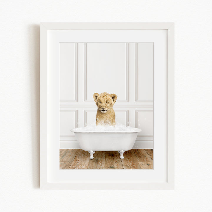 A young lion cub sitting in a white bathtub filled with water, looking up at the camera.