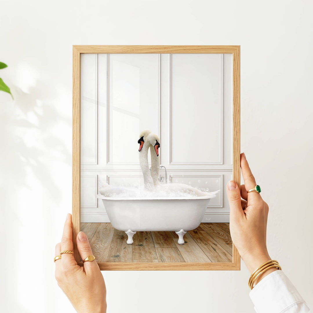 A person's hands are holding a picture frame with a photograph of a swan sitting in a bathtub.