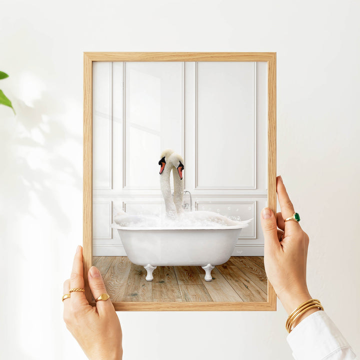 A person's hands are holding a picture frame with a photograph of a swan sitting in a bathtub.