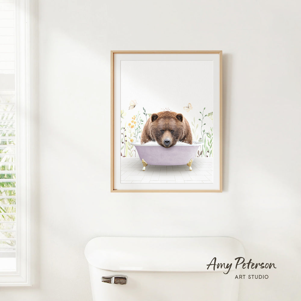 A framed illustration of a brown bear sitting in a bathtub, surrounded by flowers and plants, is hanging on a white wall.