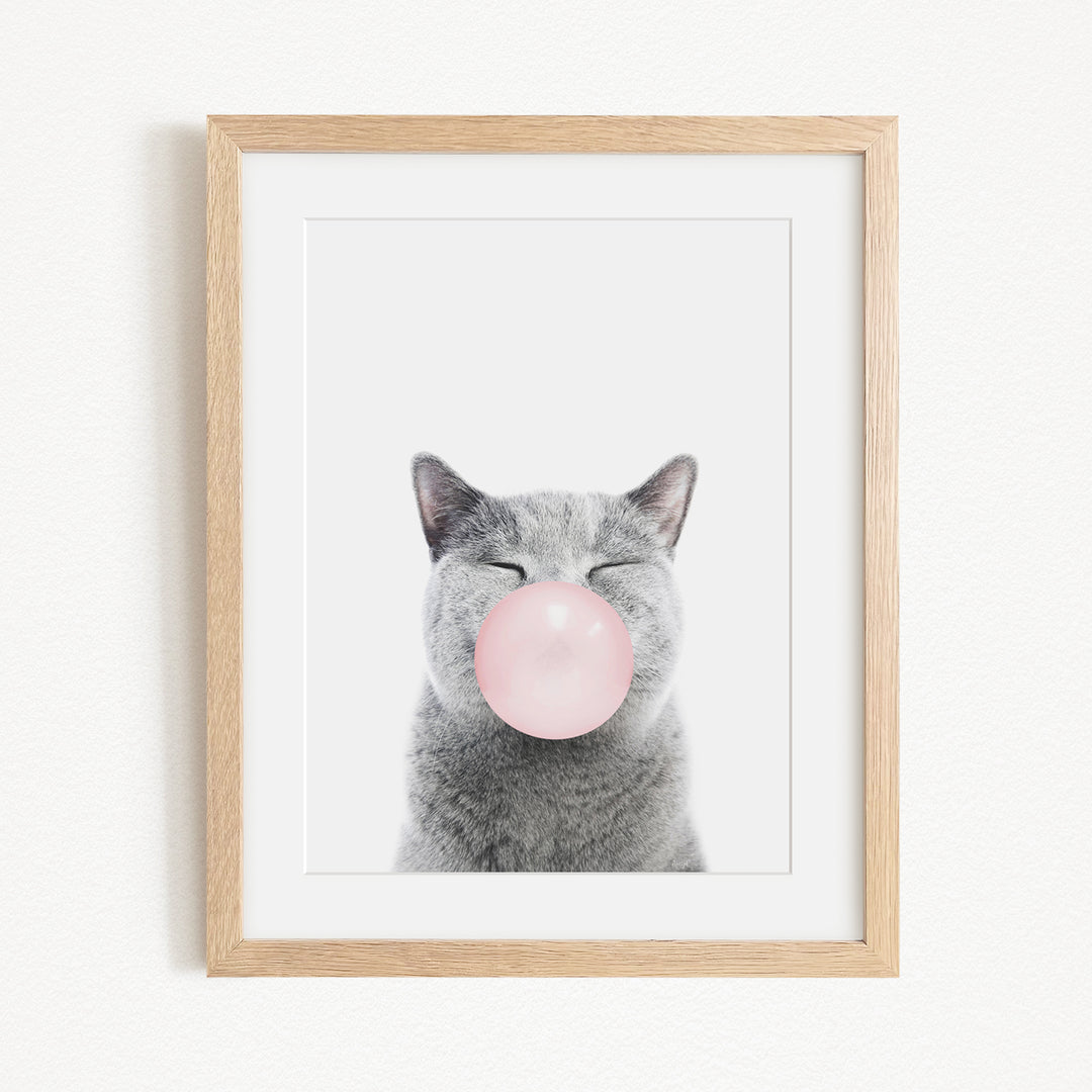 A gray cat with its eyes closed and a pink bubble blowing in its mouth, creating a whimsical and playful scene.