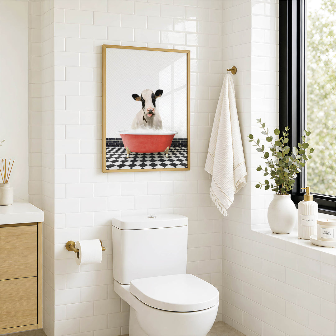 a bathroom with a white toilet, a framed picture of a cow in a red bathtub, and a towel hanging on the wall.