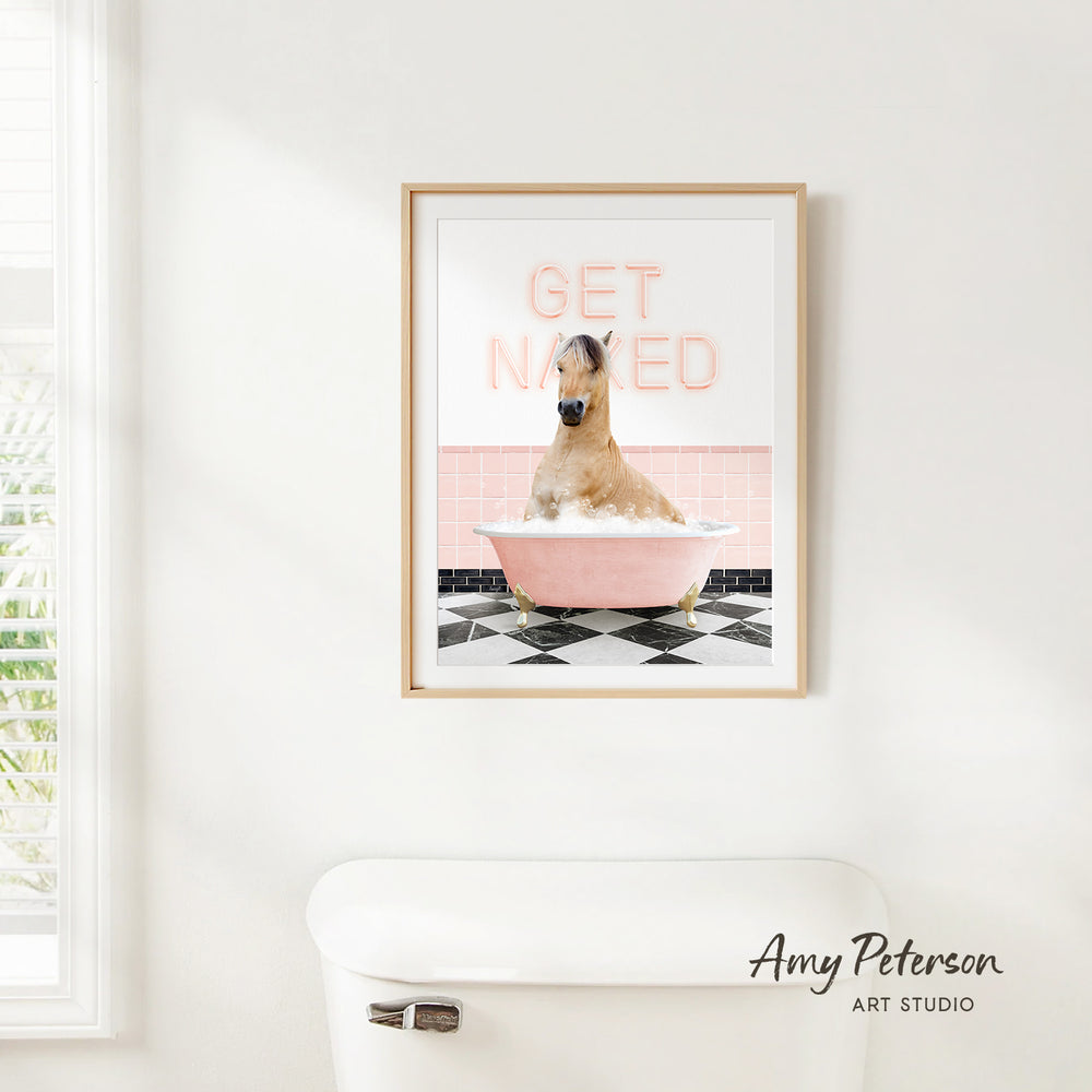 A framed print of a horse sitting in a pink bathtub with the text "GET NAKED" on it, hanging on a white wall.