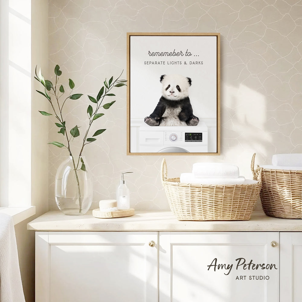 a framed poster of a panda bear sitting on a washing machine, with a wicker basket and a plant on a white countertop below it.